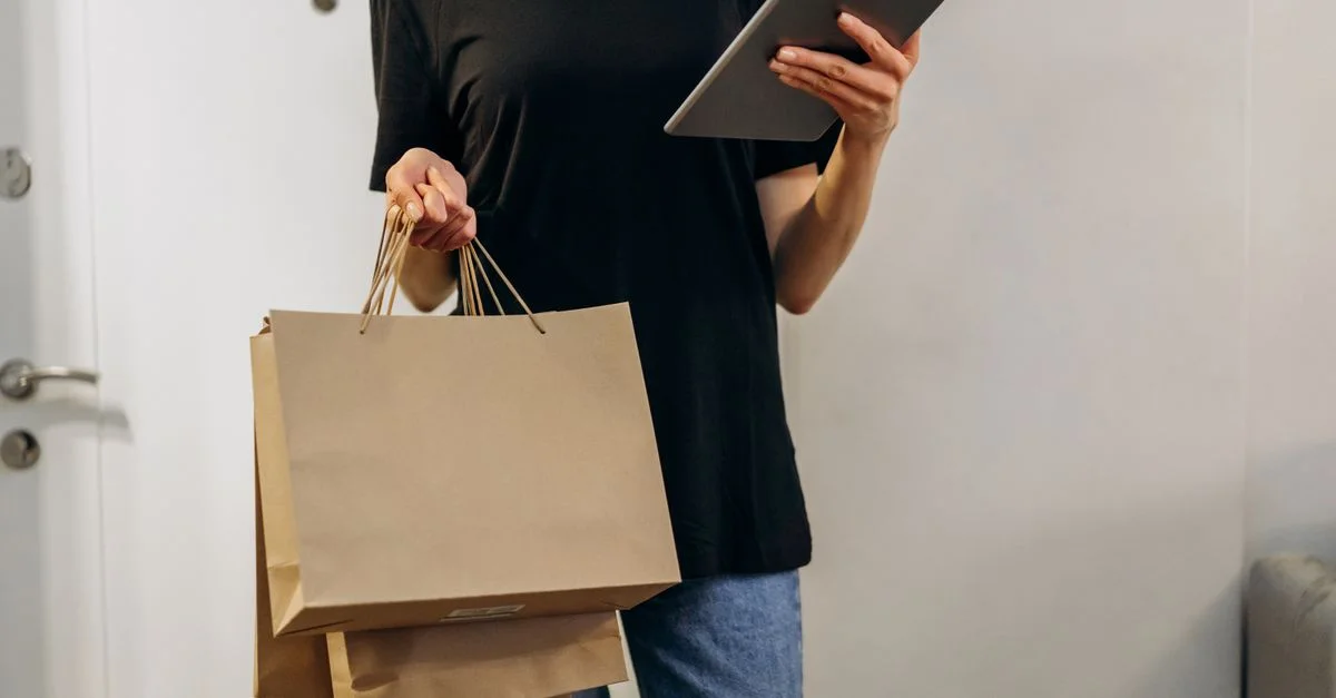 Frau in schwarzem Shirt mit Einkaufstüten, die zu Hause ein Tablet nutzt, um die Bequemlichkeit des Online-Shoppings zu symbolisieren.