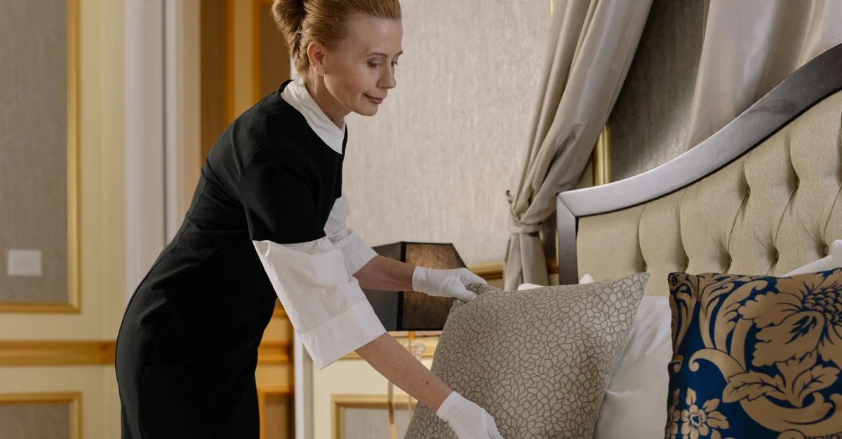 Eine uniformierte Hausdame richtet Kissen in einem luxuriösen Hotelzimmer aus und sorgt für Komfort und Sauberkeit.