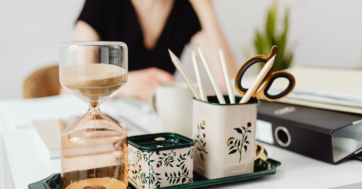 Zeitgemäße Büro-Schreibtischanordnung mit Sanduhr und floralem Schreibmaterialhalter. Ideal zur Inspiration für kreative Arbeitsbereiche.