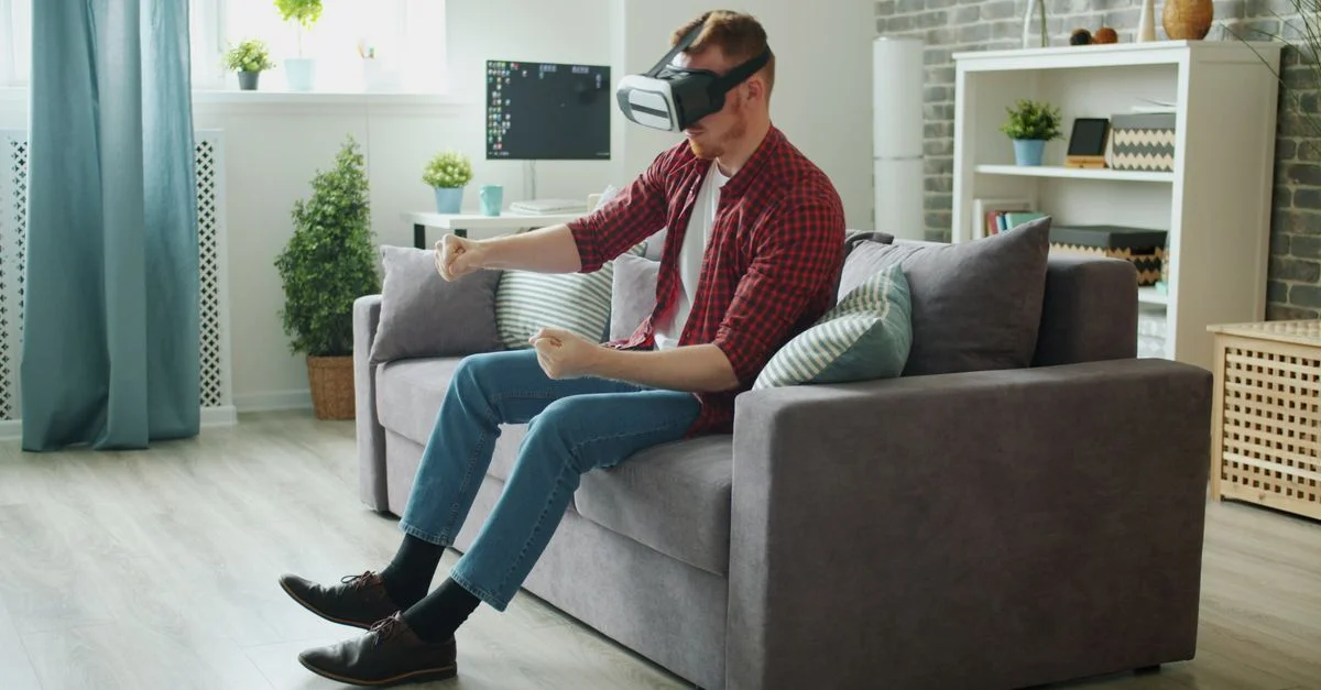 Junger Mann mit VR-Headset, der in ein virtuelles Spiel in einem modernen Wohnzimmer vertieft ist.