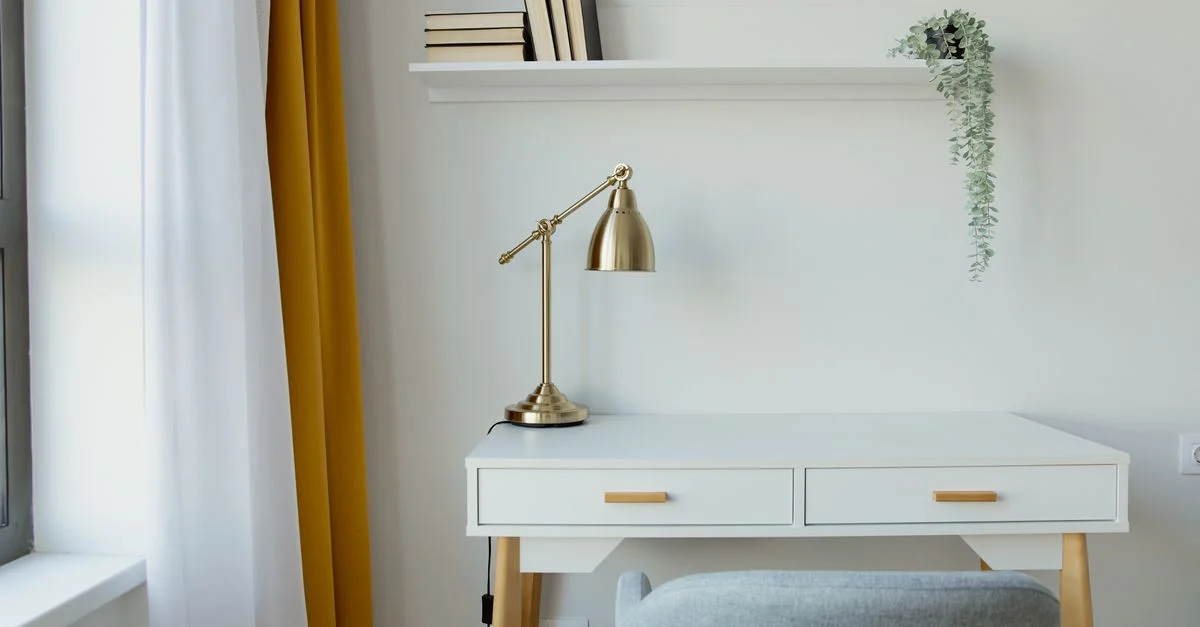 Stylischer Schreibtisch mit einer goldenen Lampe, weißer Dekoration und minimalistischem Stil.