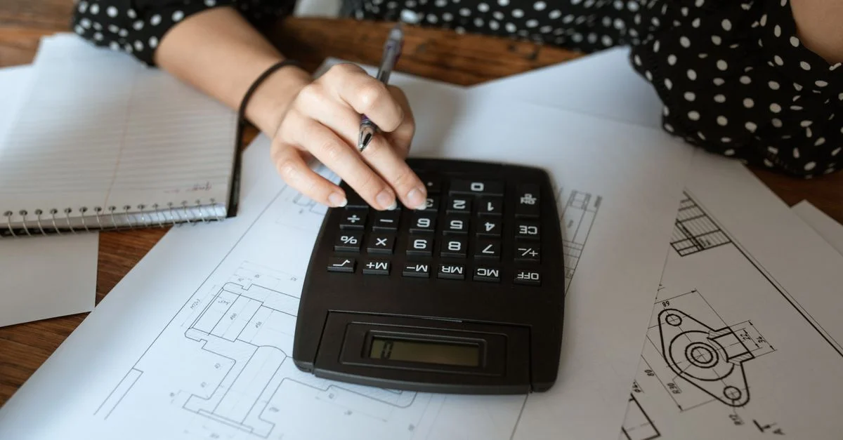 Nahaufnahme der Hand eines Architekten, die einen Taschenrechner auf technischen Zeichnungen mit einem gepunkteten Hemd verwendet.