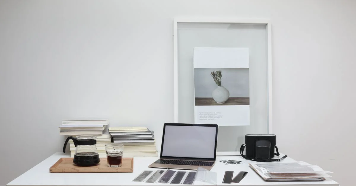 Ein zeitgemäßer Arbeitsplatz mit Vintage-Fotografieausrüstung, Büchern und Kaffee auf einem weißen Tisch.