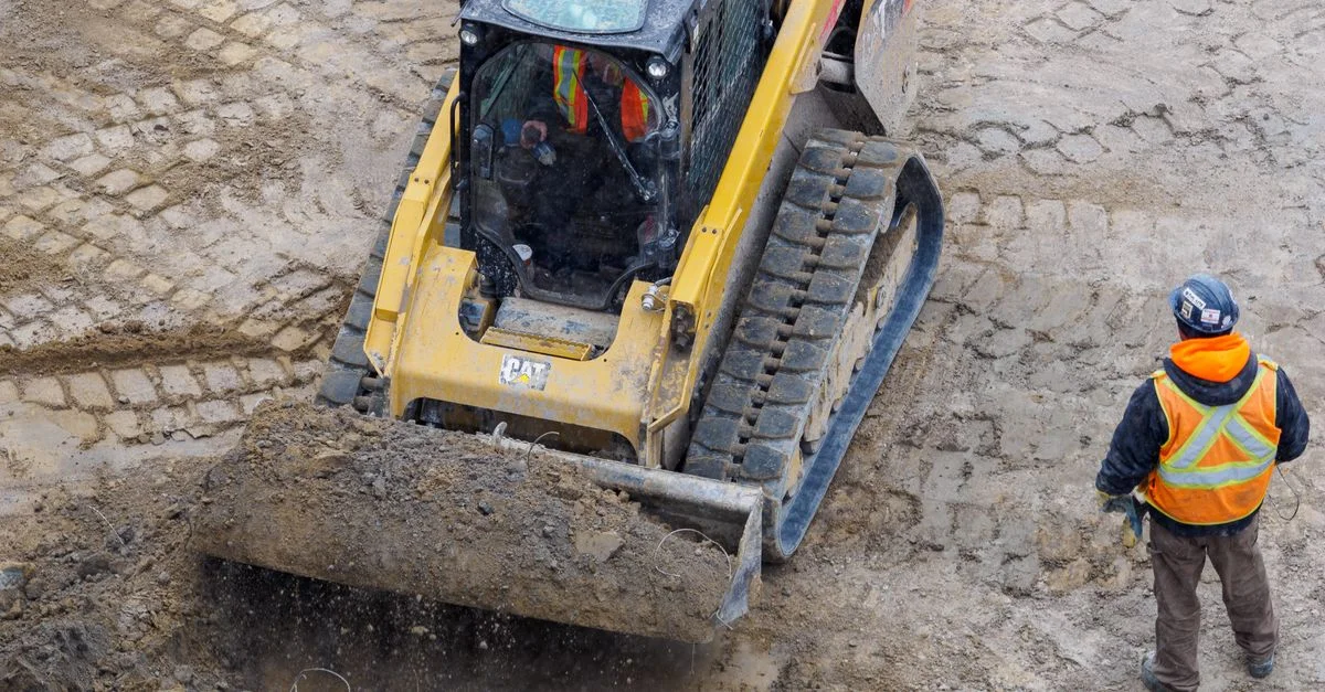 Vogelperspektive auf einen Bulldozer und einen Arbeiter auf einer Baustelle, der den Boden vorbereitet.