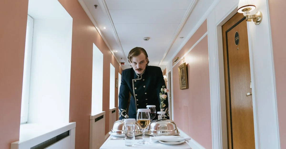 Page in Uniform präsentiert Zimmerservice in einem Hotelflur.