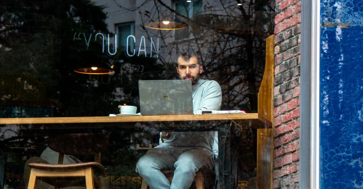 Junger Mann arbeitet am Laptop in einem Café, durch das Fenster betrachtet. Gemütliche Innenatmosphäre.