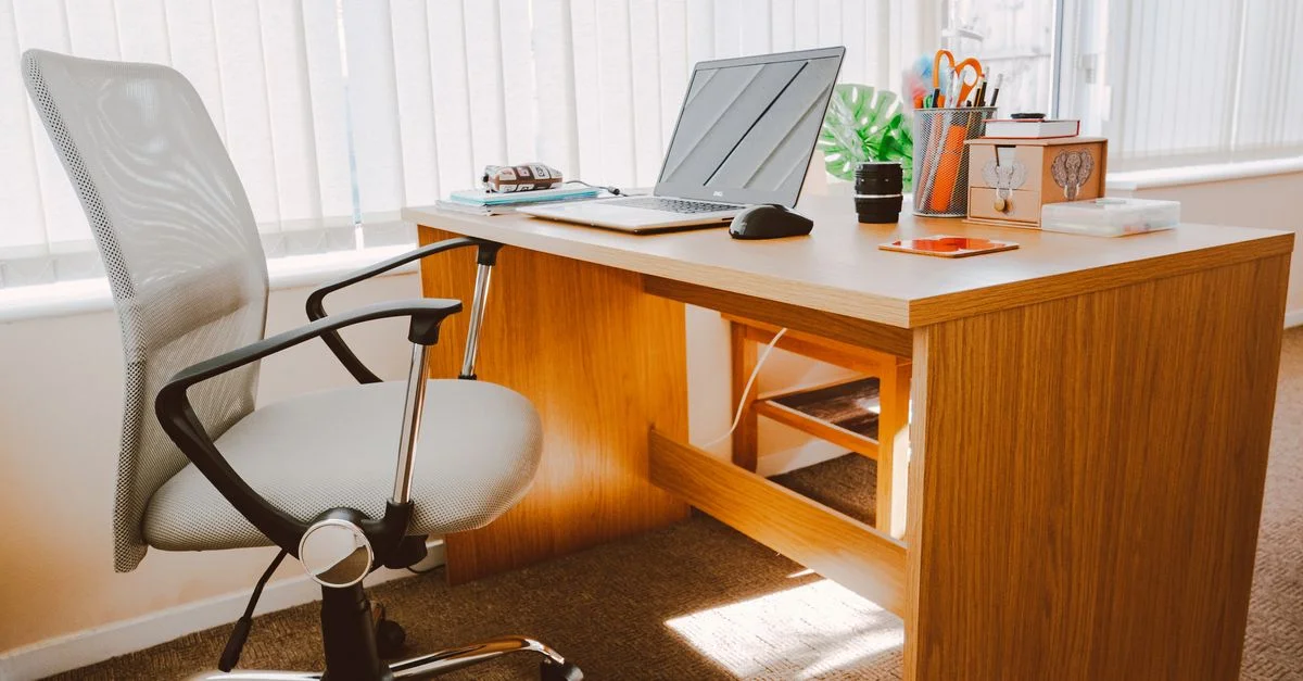 Ein modernes Büroarbeitsplatz mit einem Holztisch, Stuhl, Laptop und hellem natürlichem Licht.