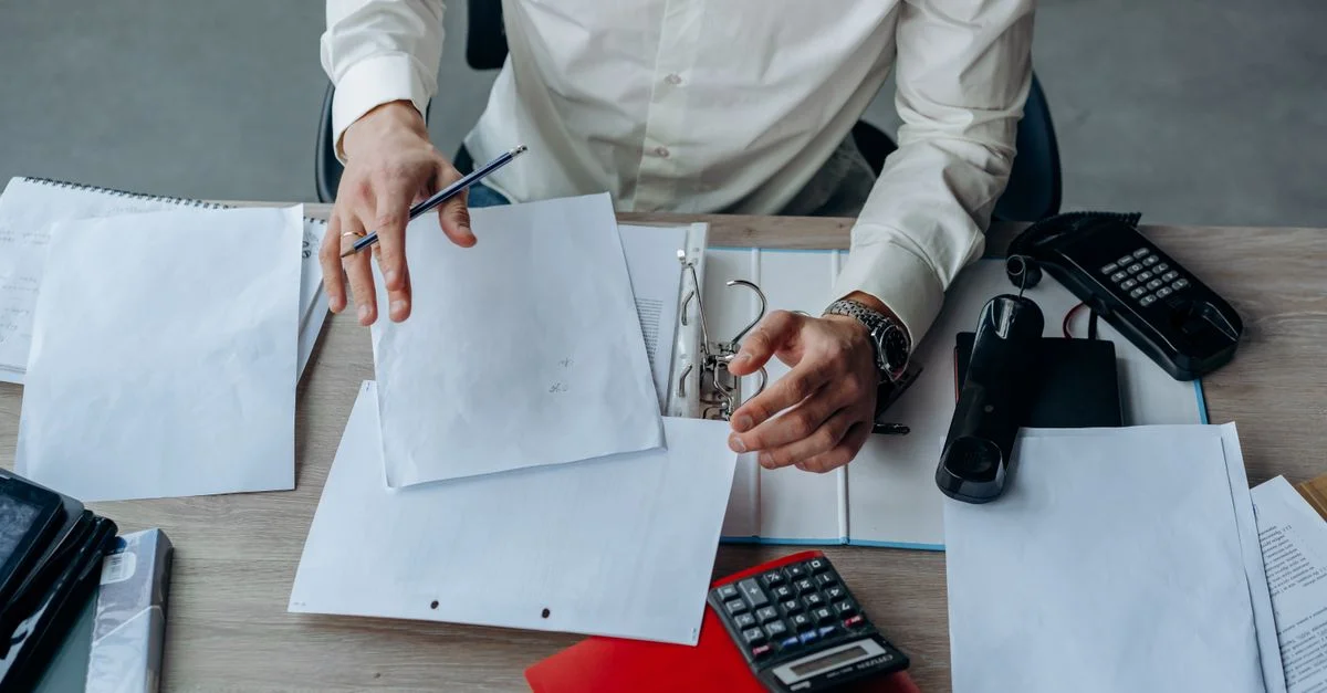Ein Business-Profi organisiert Dokumente an einem geschäftigen Bürotisch und betont die Produktivität.