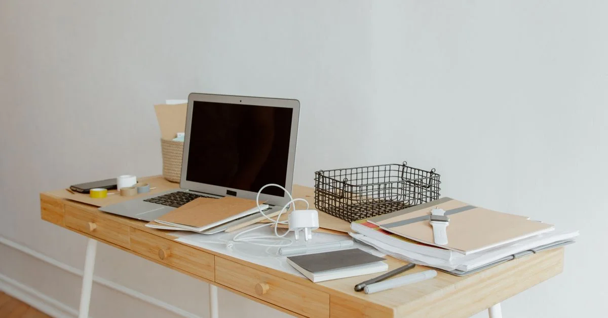 Ein ordentlich organisierter Schreibtisch mit einem Laptop, Notizbüchern und Büromaterialien in einem minimalistischen Büro.